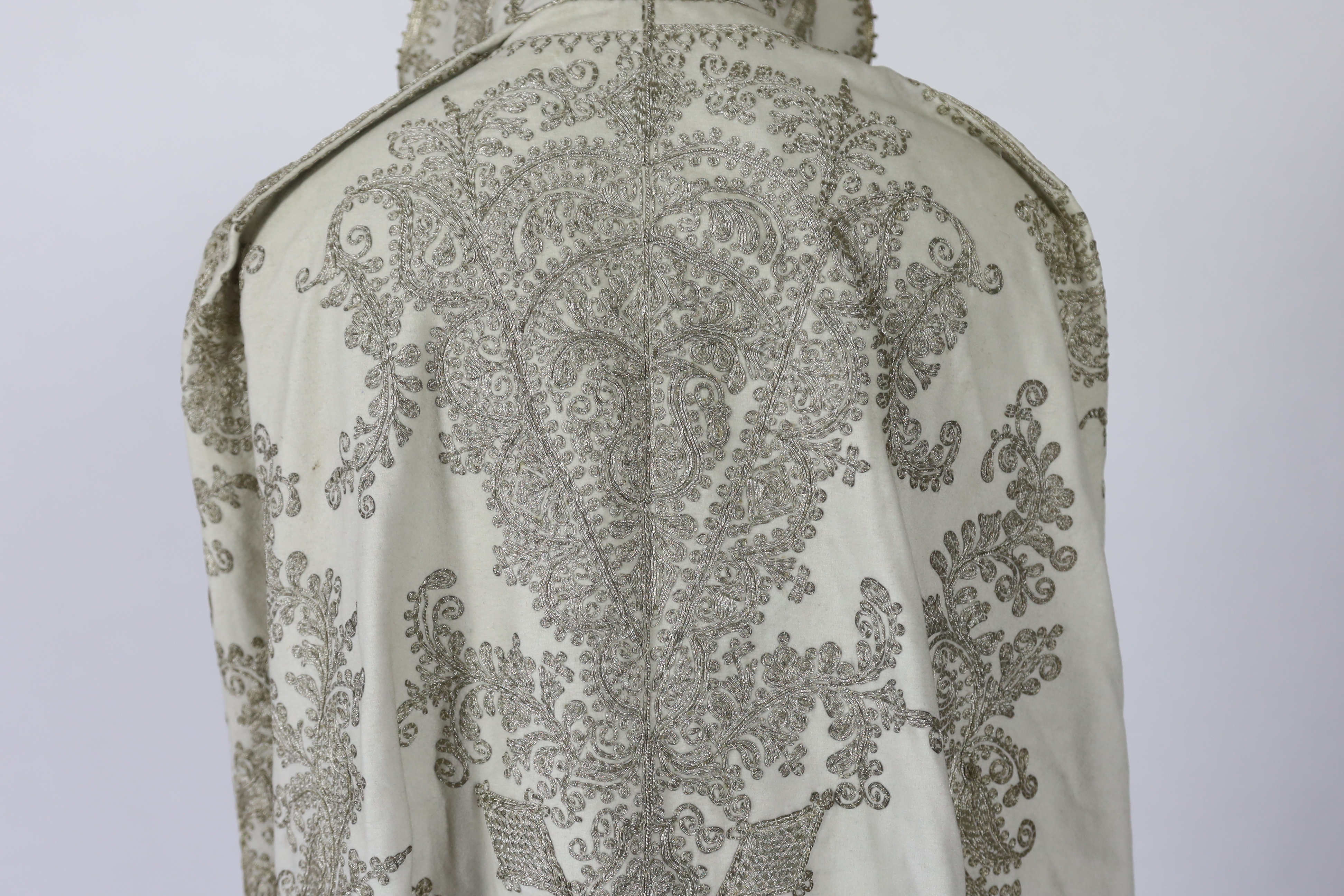 A 19th century Indian fine cream wool embroidered cape, probably made for the European market, embroidered in panels of silver metallic thread in an ornate vertical design with turquoise embellishments and lined in black